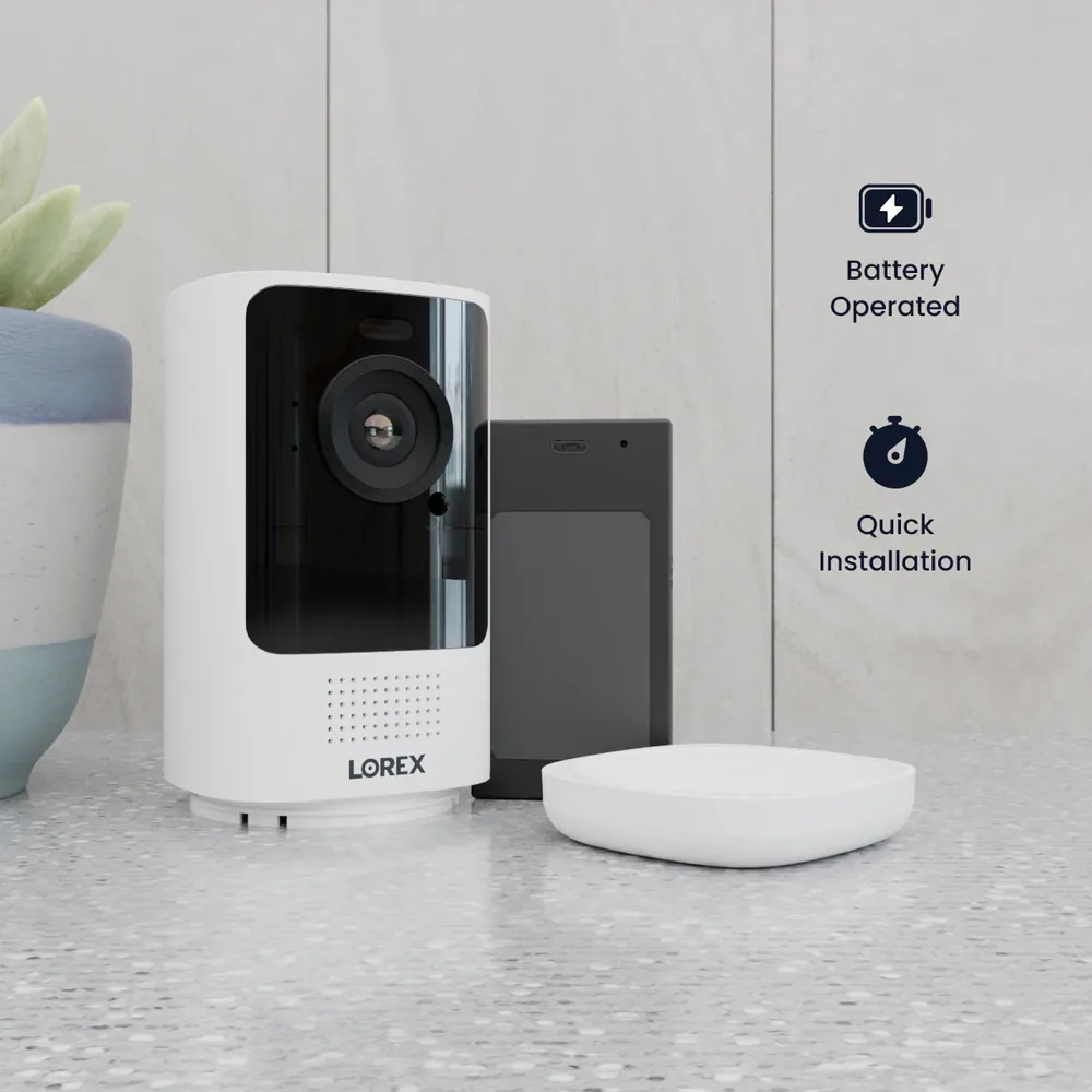 White Lorex security camera on a speckled surface, next to a plant and a small device. Text reads "Battery Operated" and "Quick Installation."